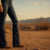Dark wash bootcut jeans over brown cowboy boots at golden hour in open country