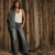 Fashion editorial: woman in kick-boot denim, white tank, concho belt, and boots against a barn wall at golden hour