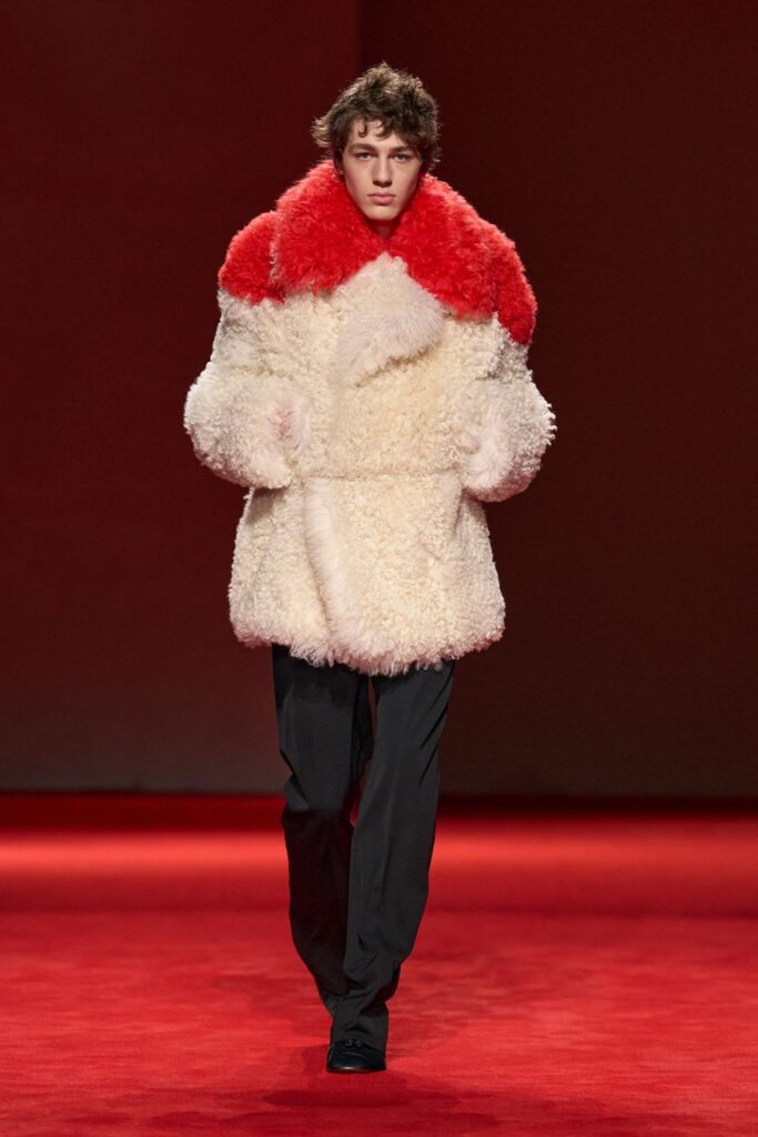 Bottega Veneta Fall 2026 look 43: a hip-length shaggy cream jacket with a red shaggy collar, worn over slim black trousers and black shoes