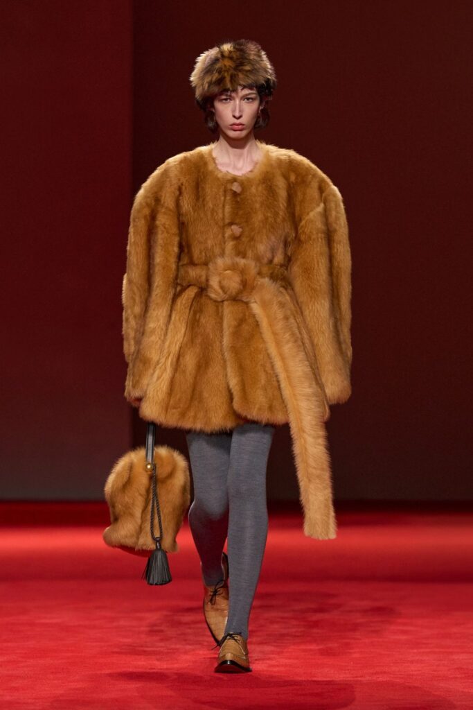 Bottega Veneta Fall 2026 look 49: a belted camel shaggy coat with a matching hat and bag, worn with grey tights and tan shoes