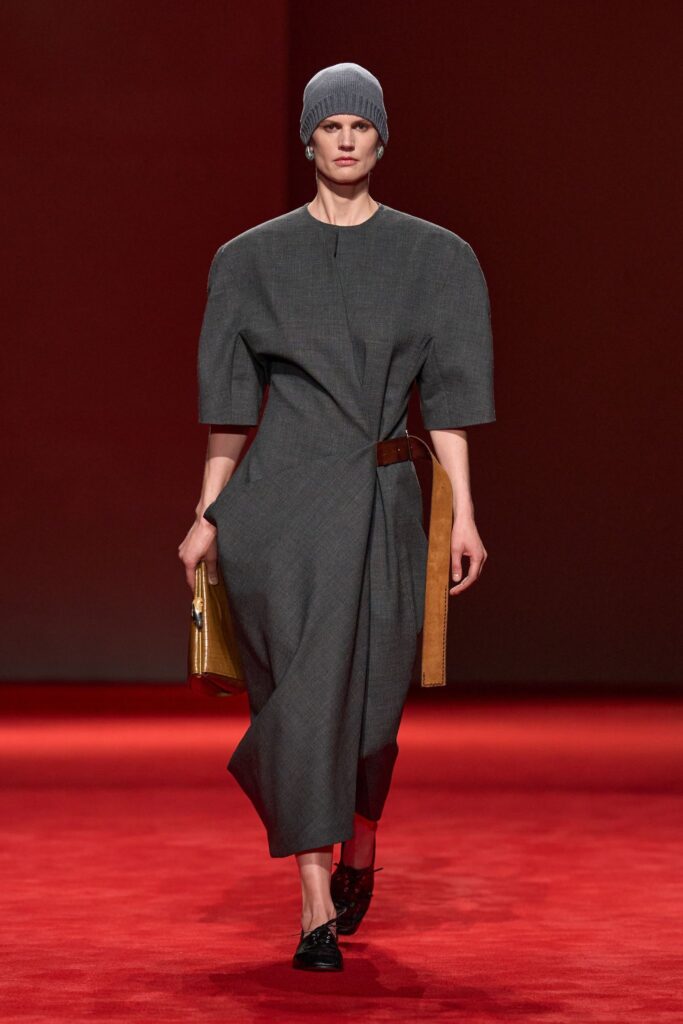 Bottega Veneta Fall 2026 look 4: a grey wool wrap look with rounded shoulders, cinched by a long brown leather belt
