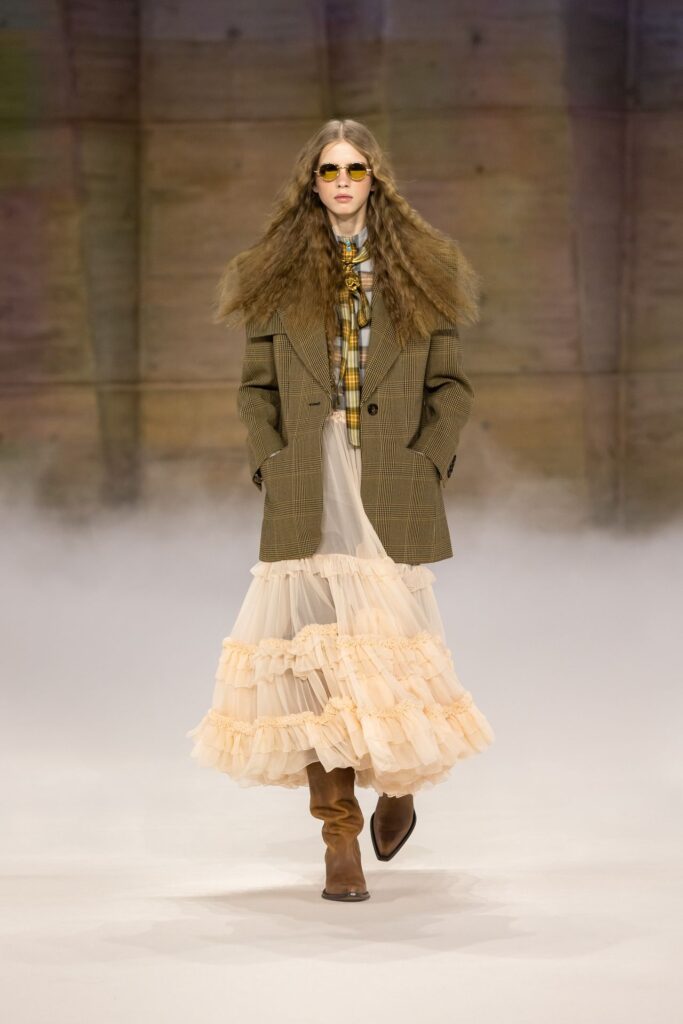 Chloé Fall 2026 look 4: an olive jacket over a sheer cream tiered skirt, worn with brown boots