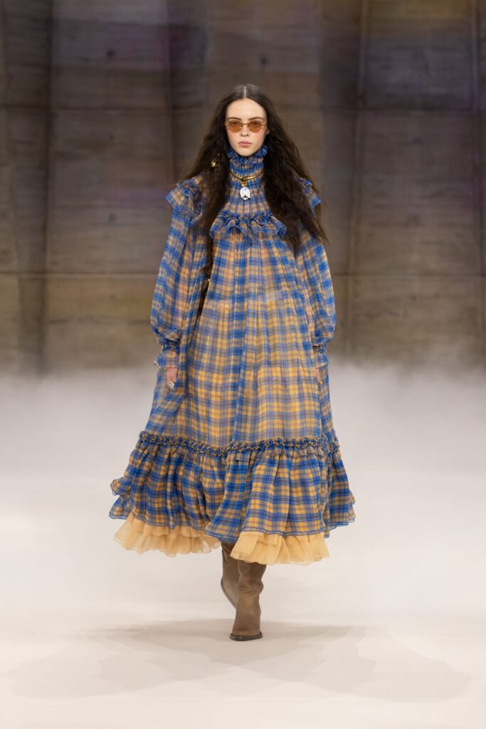 Chloé Fall 2026 look 6: blue and yellow plaid tiered dress with a ruffled hem and brown boots