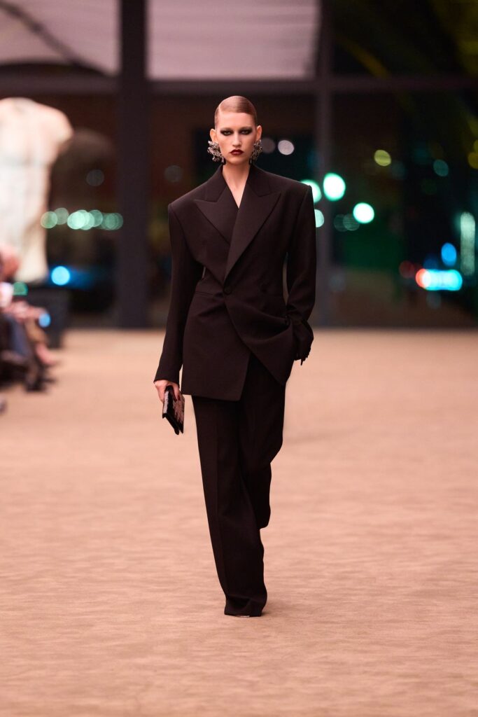 Saint Laurent Fall 2026 look 36: long black single-breasted jacket with sloped shoulders over wide black trousers