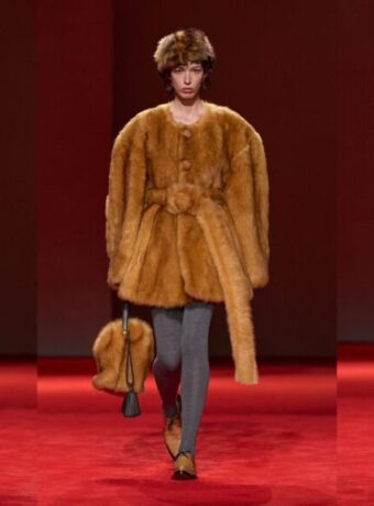 Shearling coat outfit ideas from Bottega Veneta Fall 2026: a shaggy cream jacket with a red collar over black trousers, a belted camel shaggy coat with grey tights, and a long cream shaggy coat with a camel belt (looks 43, 49 and 40)