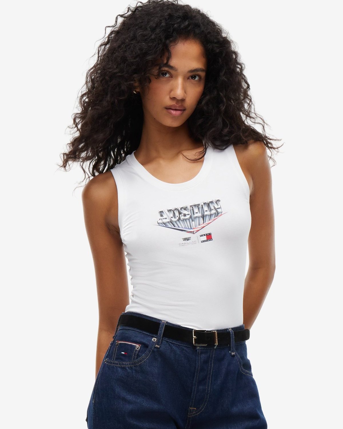 Model in the white Tommy Hilfiger x Cadillac F1 Team women's Austin tank with dark jeans and a black belt