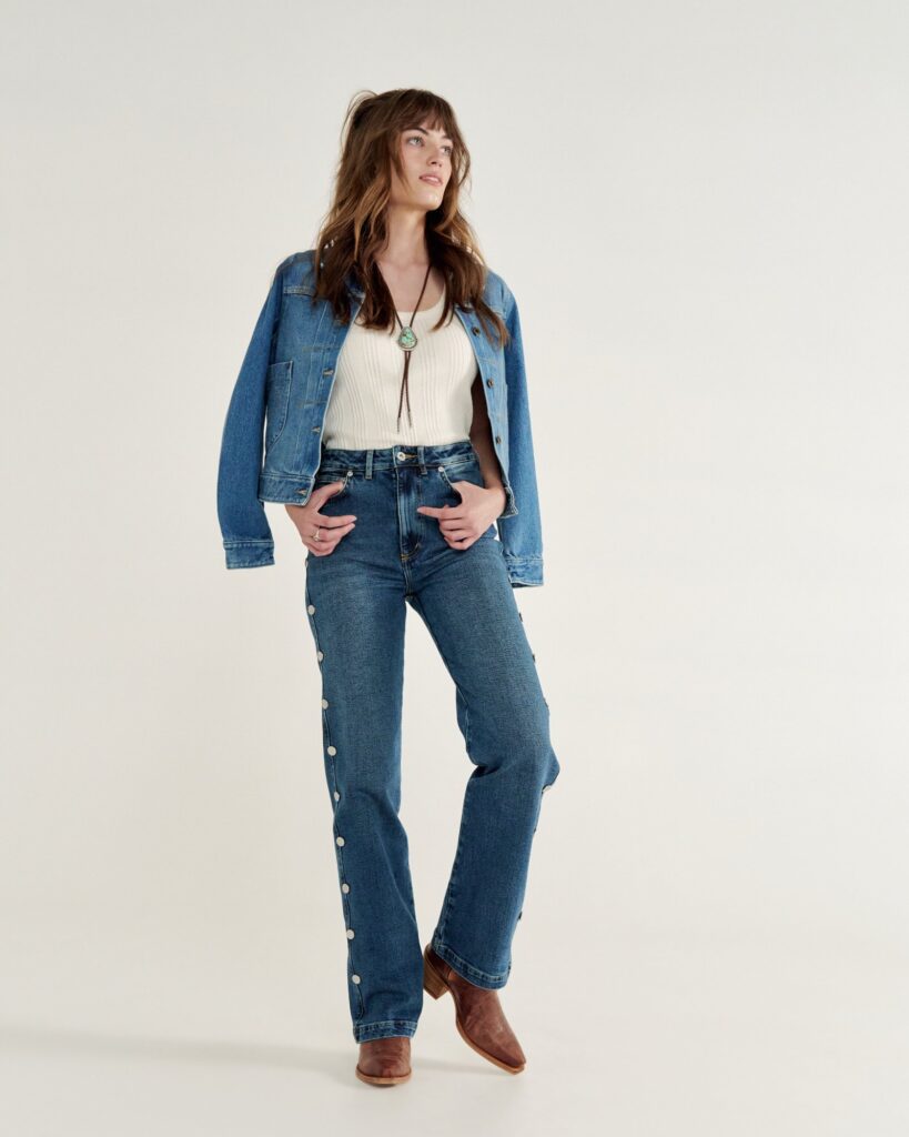 Denim jacket over a cream knit top with a bolo tie, high-rise jeans and brown cowgirl boots