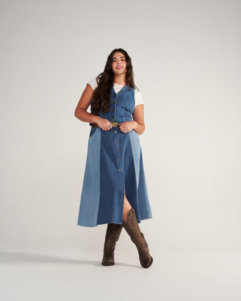 Sleeveless denim midi dress over a white tee with a belt and brown cowgirl boots