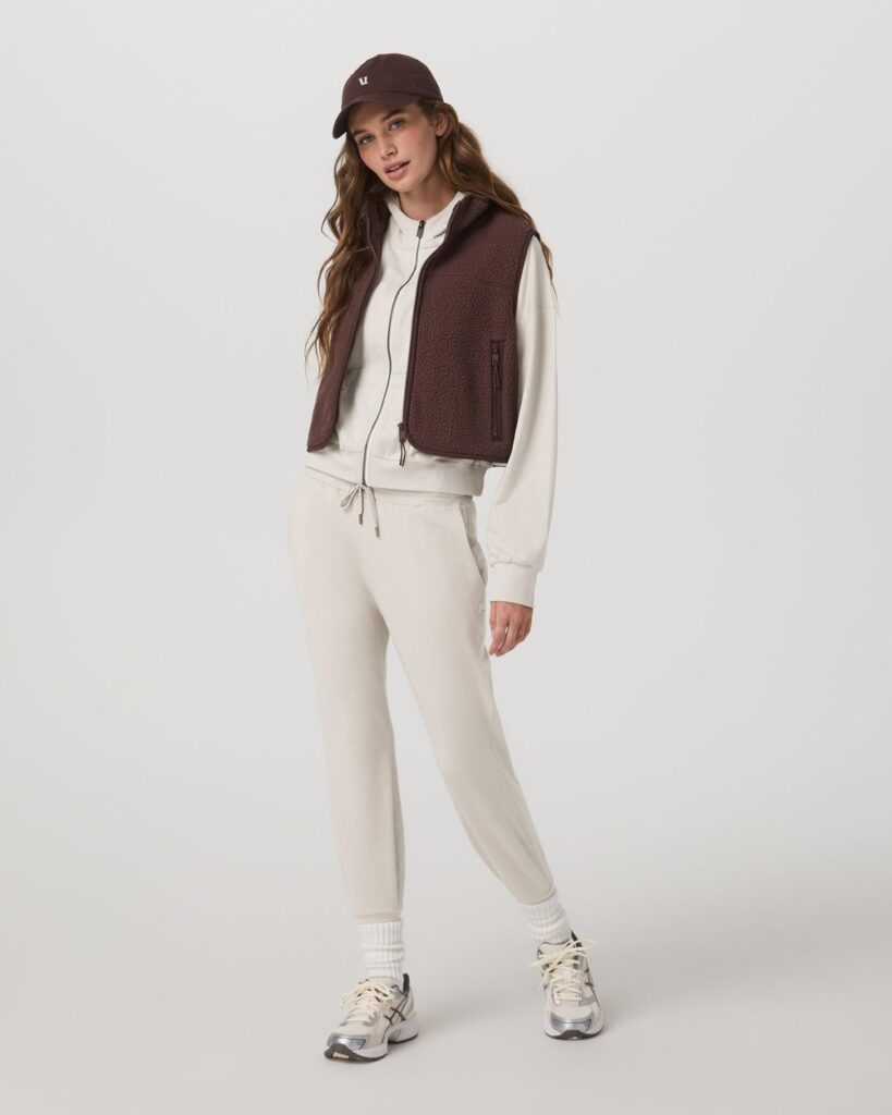 Vuori women's Performance Jogger in ecru heather, a cropped tapered DreamKnit jogger, worn with a brown vest and sneakers